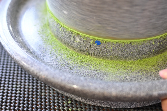 灰色の石の挽き臼で抹茶を挽いている。挽かれた緑の抹茶の粉が臼にのっている。